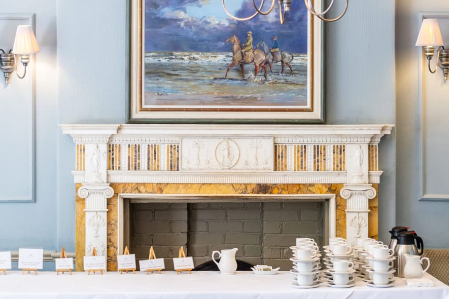 Ornate fireplace with artwork above, set with stacked teacups and saucers ready for a classic afternoon tea.