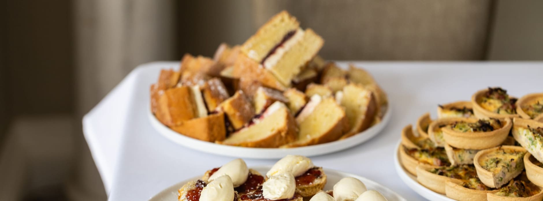 Afternoon tea spread with scones, Victoria sponge cake, and savoury tartlets on a white table.