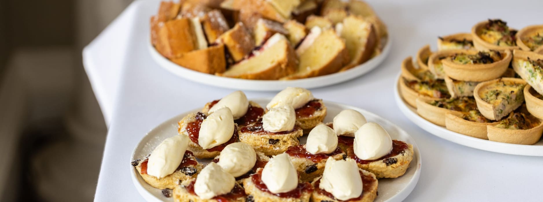 Afternoon tea spread with scones, Victoria sponge cake, and savoury tartlets on a white table.