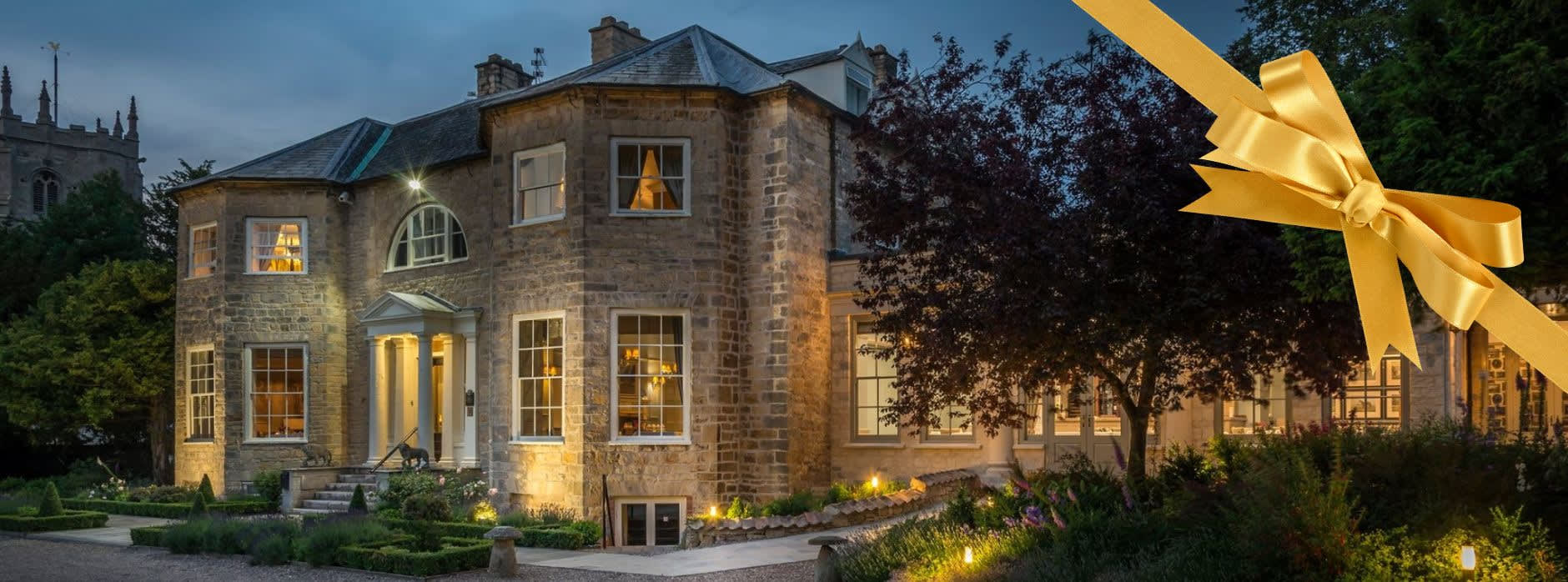 Washingborough Hall Hotel at dusk, a grand Georgian manor softly lit with warm lights, surrounded by gardens, with a golden ribbon graphic overlaid on the image.