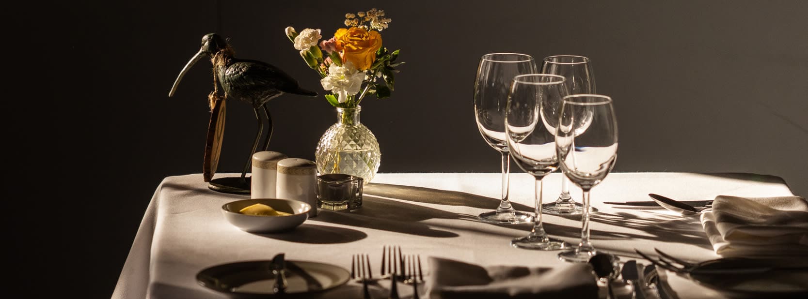 Close-up of elegant table setting with wine glasses, linen napkins, and polished cutlery in warm, golden light.