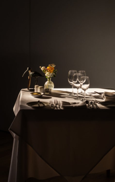 Close-up of elegant table setting with wine glasses, linen napkins, and polished cutlery in warm, golden light.