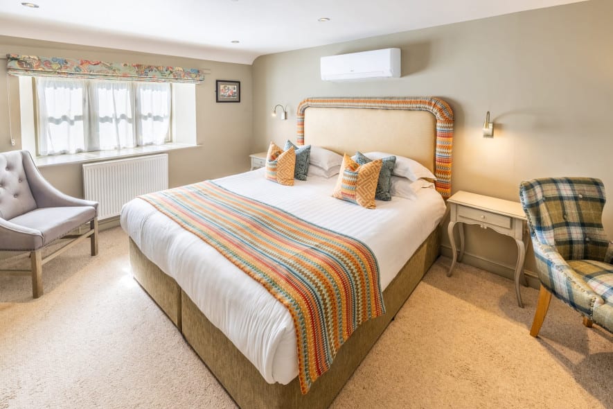 A double bed with colorful cushions and a striped throw, flanked by soft chairs in a classic double bedroom at Washingborough Hall Hotel.