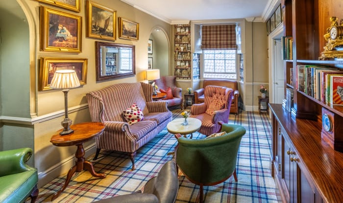Cosy lounge with striped sofas, armchairs, tartan carpet, bookcase and framed artwork creating a classic drawing-room feel.