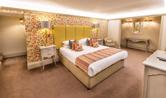 Country-house bedroom with super king bed, yellow headboard, floral wallpaper, bedside lamps and dressing table.