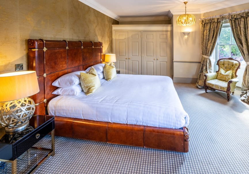 Spacious Superior Ingilby Room at Washingborough Hall with leather framed bed, gold cushions, armchair by the window and fitted wardrobes.