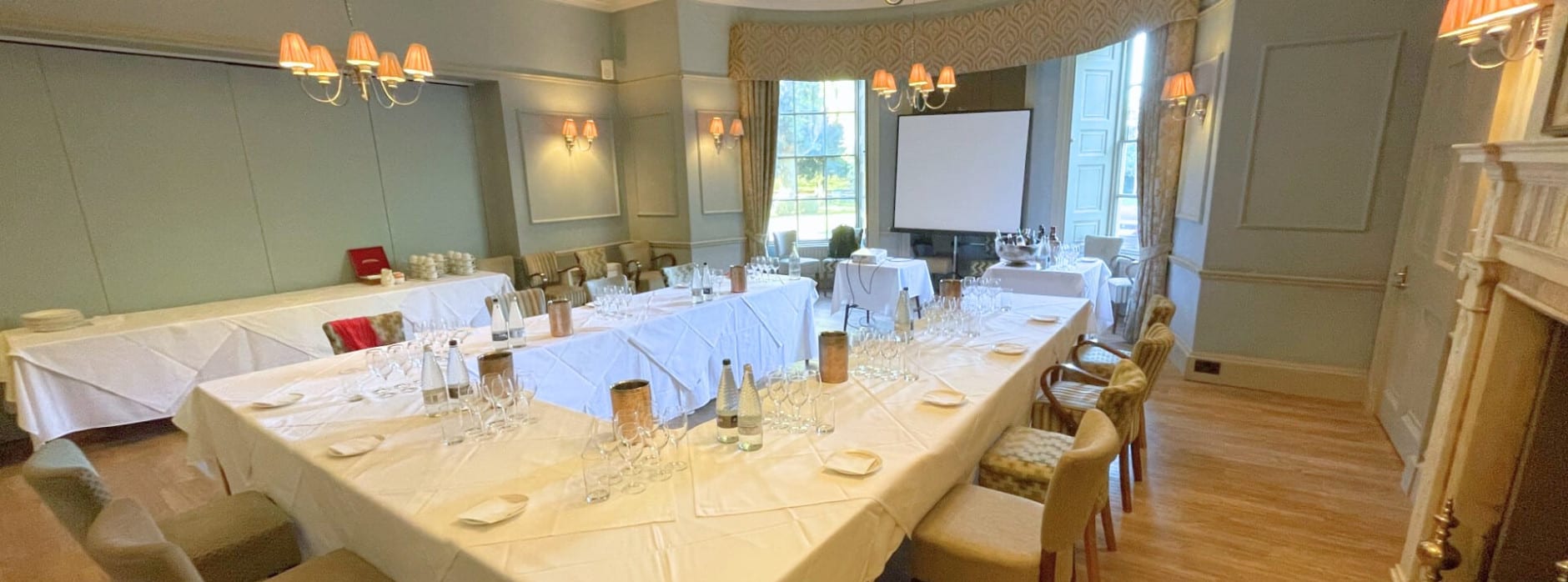 Corporate meeting room at Washingborough Hall Hotel in Lincoln with U-shaped tables, white linens, glassware and a presentation screen set for a business event.