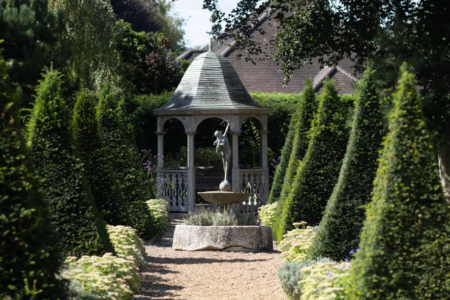 Garden pathway at Washingborough Hall Hotel leading to a gazebo with a fountain, lined with conical evergreens and flowering borders.