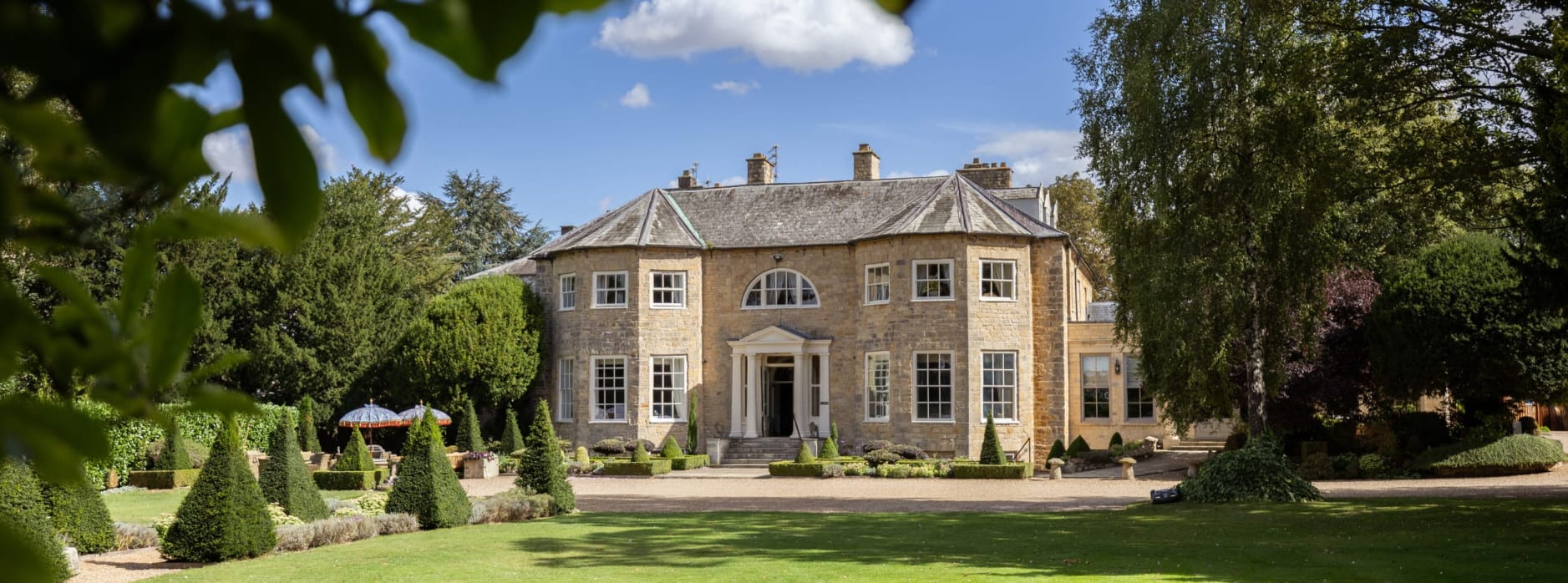 Washingborough Hall Hotel, a grand Georgian manor with curved wings and a columned entrance, set among lawns, trees, and neatly clipped topiary.