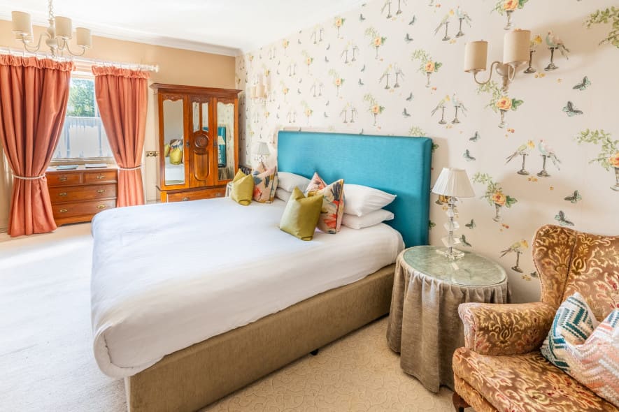A luxurious room, featuring a large bed with a blue headboard, elegant wall paper and deep red curtains.