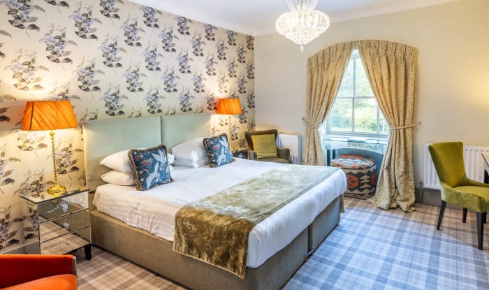 Stylish bedroom with floral wallpaper, mirrored tables, and soft gold and green furnishings.
