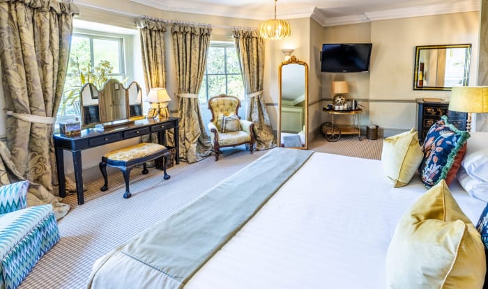 Bright, elegant bedroom with gold accents, vanity, armchair, and full‑length mirror.