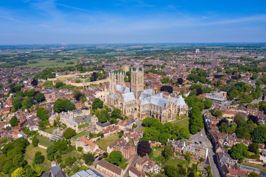Aerial view of Lincoln Cathedral surrounded by historic buildings and greenery under a clear blue sky.