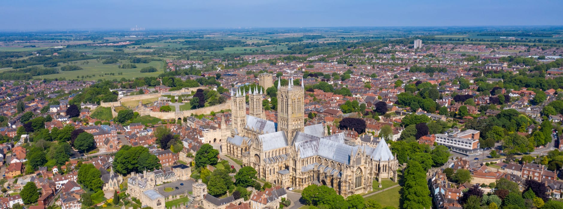Aerial view of Lincoln Cathedral surrounded by historic buildings and greenery under a clear blue sky.