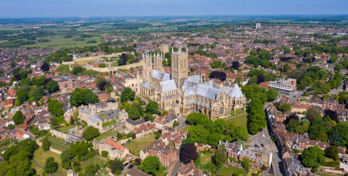 Aerial view of Lincoln Cathedral surrounded by historic buildings and greenery under a clear blue sky.