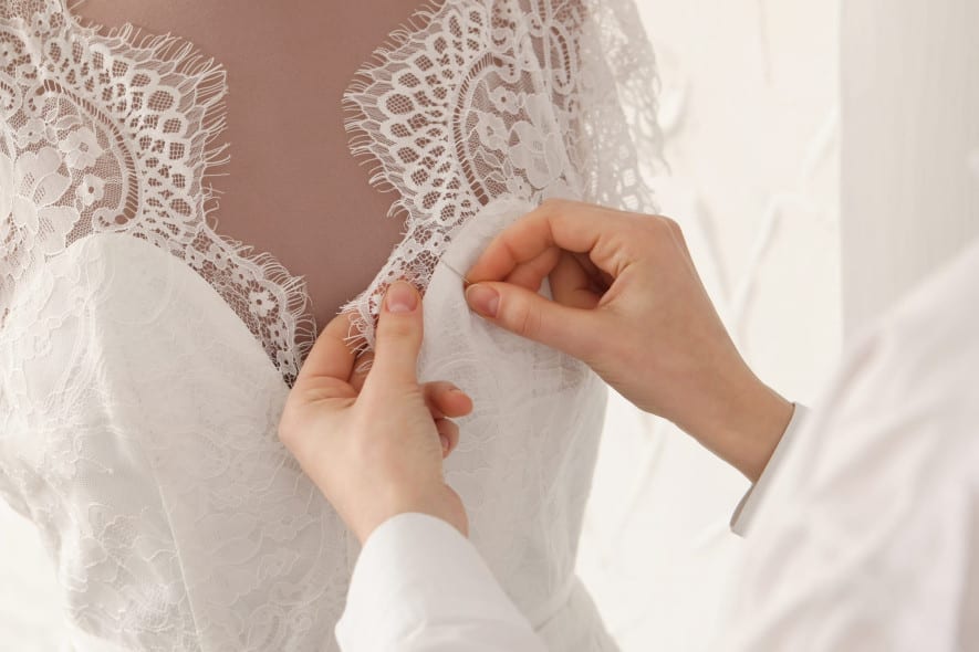 A close-up of a seamstress adjusting delicate lace on a white wedding dress, carefully stitching the fabric on a mannequin to perfect the intricate details.