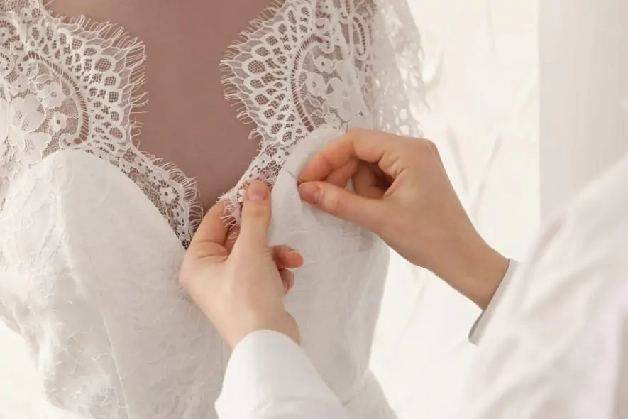 A close-up of a seamstress adjusting delicate lace on a white wedding dress, carefully stitching the fabric on a mannequin to perfect the intricate details.