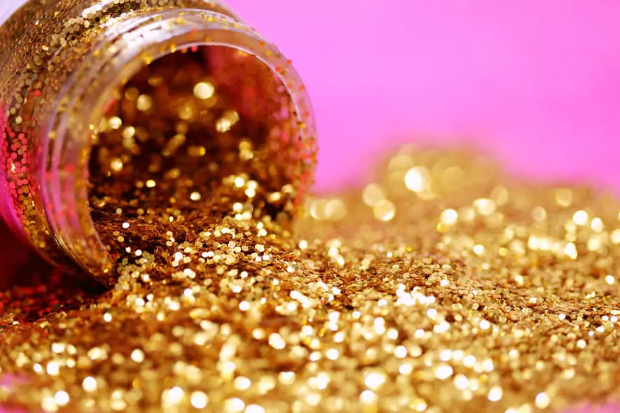 Gold glitter is spilling out of a plastic pit, with a pink background