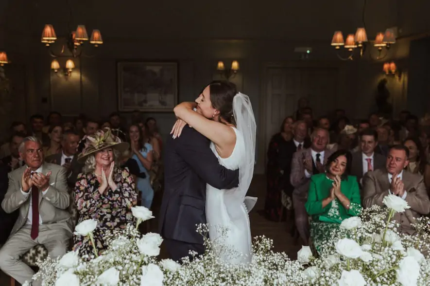 Bride and groom share a joyful embrace during their indoor ceremony at Washingborough Hall, surrounded by guests and white florals.