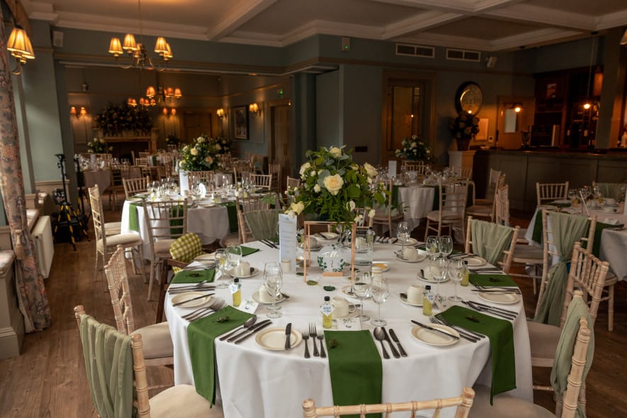 Wedding breakfast room at Washingborough Hall Hotel, set with round tables, white linens, green accents and floral centrepieces.