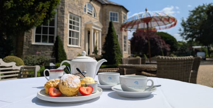 Afternoon tea with scones, strawberries and tea set on a white tablecloth in the sunny gardens of Washingborough Hall Hotel.