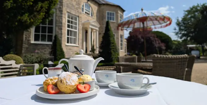 Afternoon tea with scones, strawberries and tea set on a white tablecloth in the sunny gardens of Washingborough Hall Hotel.