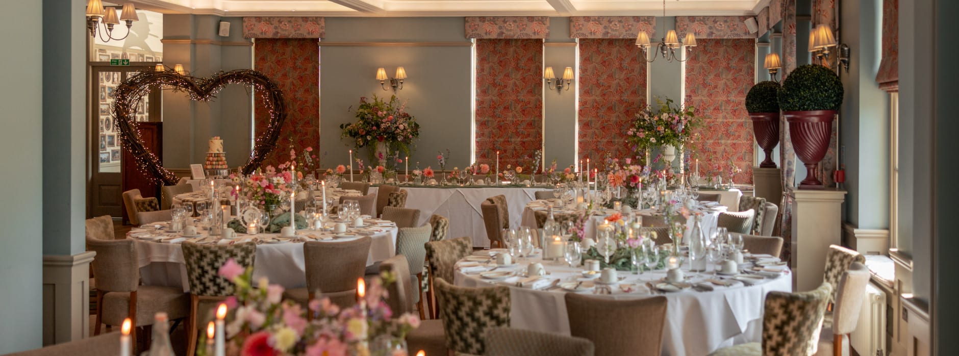 Romantic wedding reception with floral centrepieces, candles, elegant round tables, and a heart-shaped light feature in a refined venue.